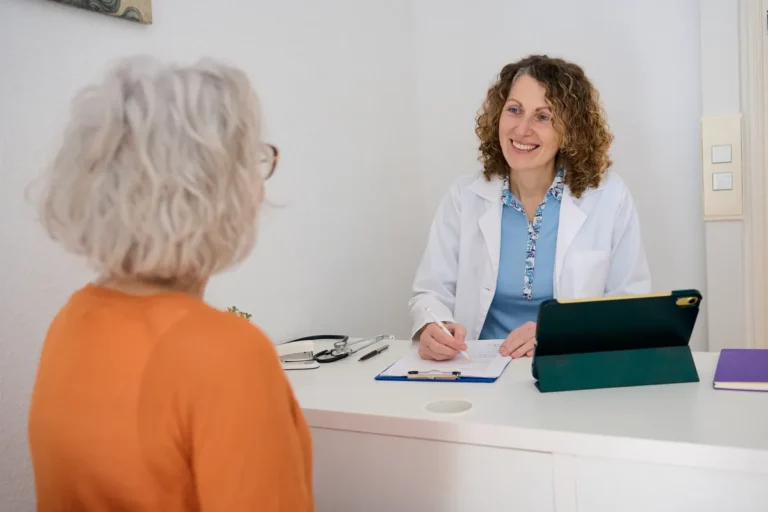 Smiling female doctor taking notes while talking with a grey-haired patient in her office