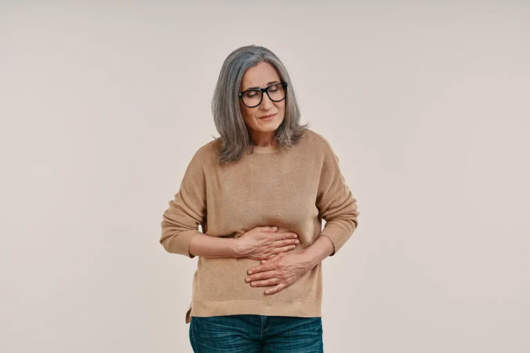 Mature woman with grey hair and glasses holding her stomach with both hands