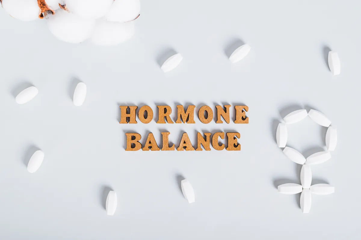 Wooden letters spelling hormone balance next to white pills arranged as a female symbol
