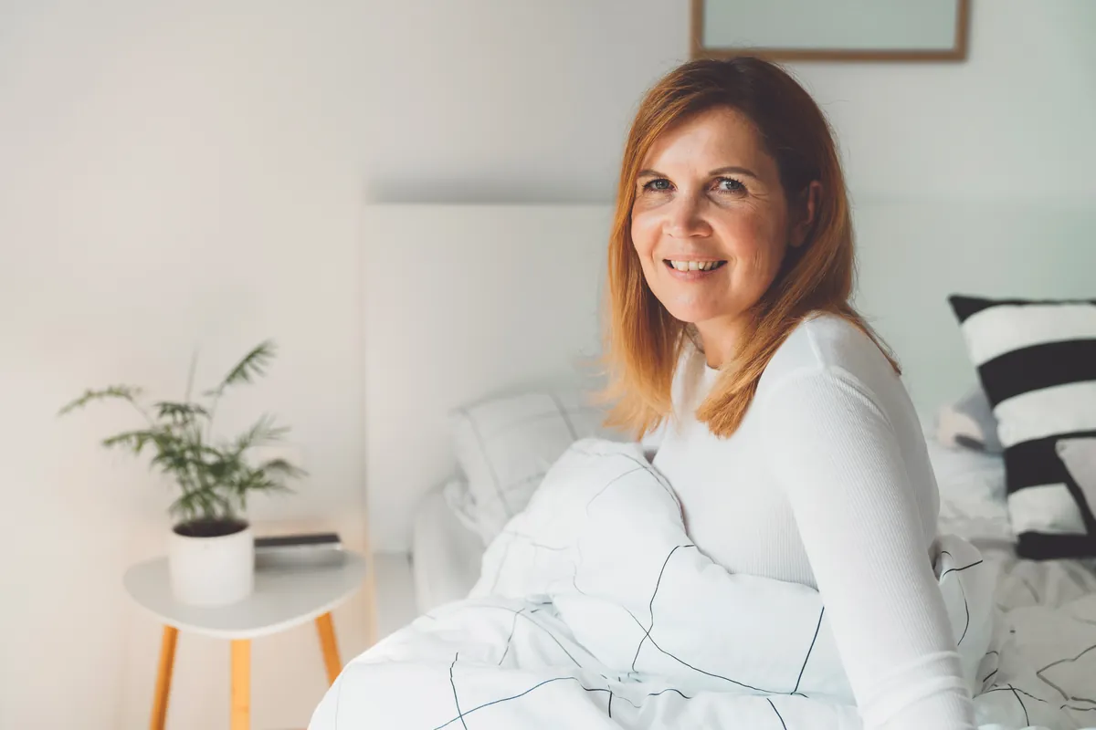 Smiling woman sitting upright in bed with white pillows around her