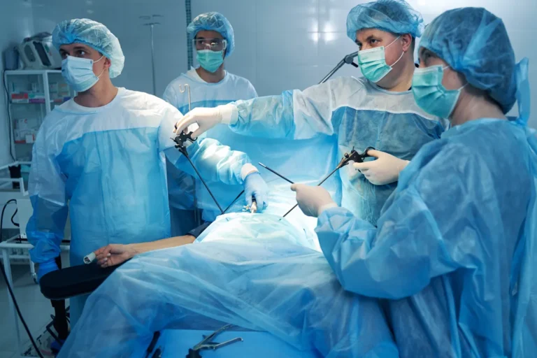 Surgical team in blue gowns, caps and masks holding long, thin laparoscopic instruments over a patient covered with sterile drapes