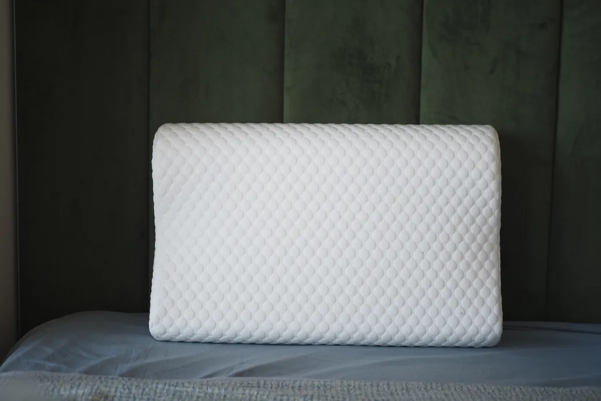 White pillow with a textured cover on a bed against a dark green headboard