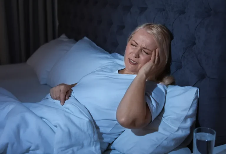 Woman in her 50s lying awake in bed at night, holding her head and wincing