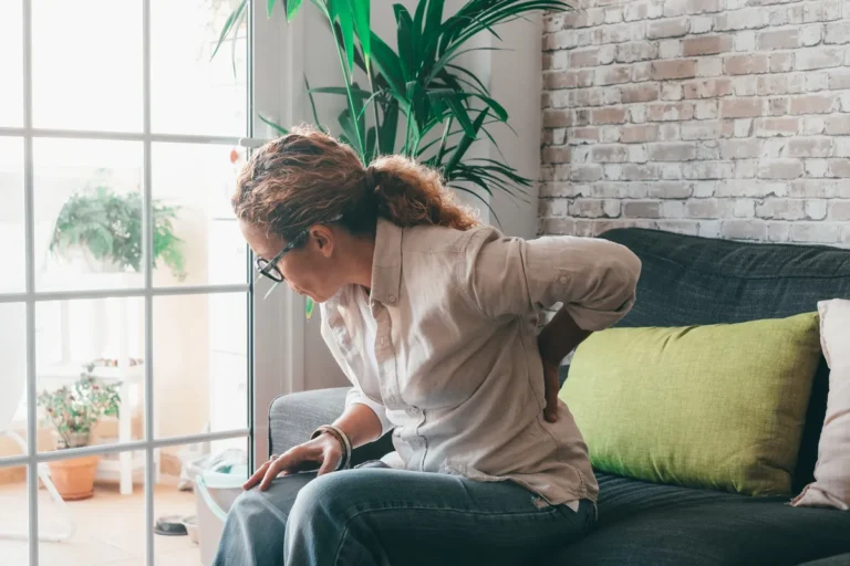 Woman sitting on a sofa with one hand on her lower back
