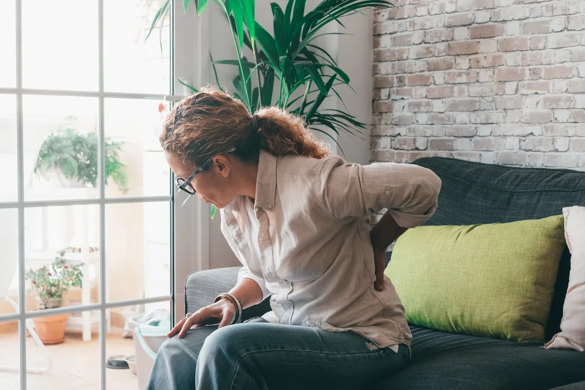 Woman sitting on a sofa with one hand on her lower back