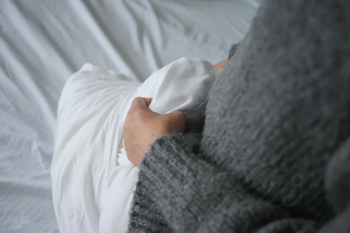 Woman in a gray sweater holding a pillow against her abdomen for support