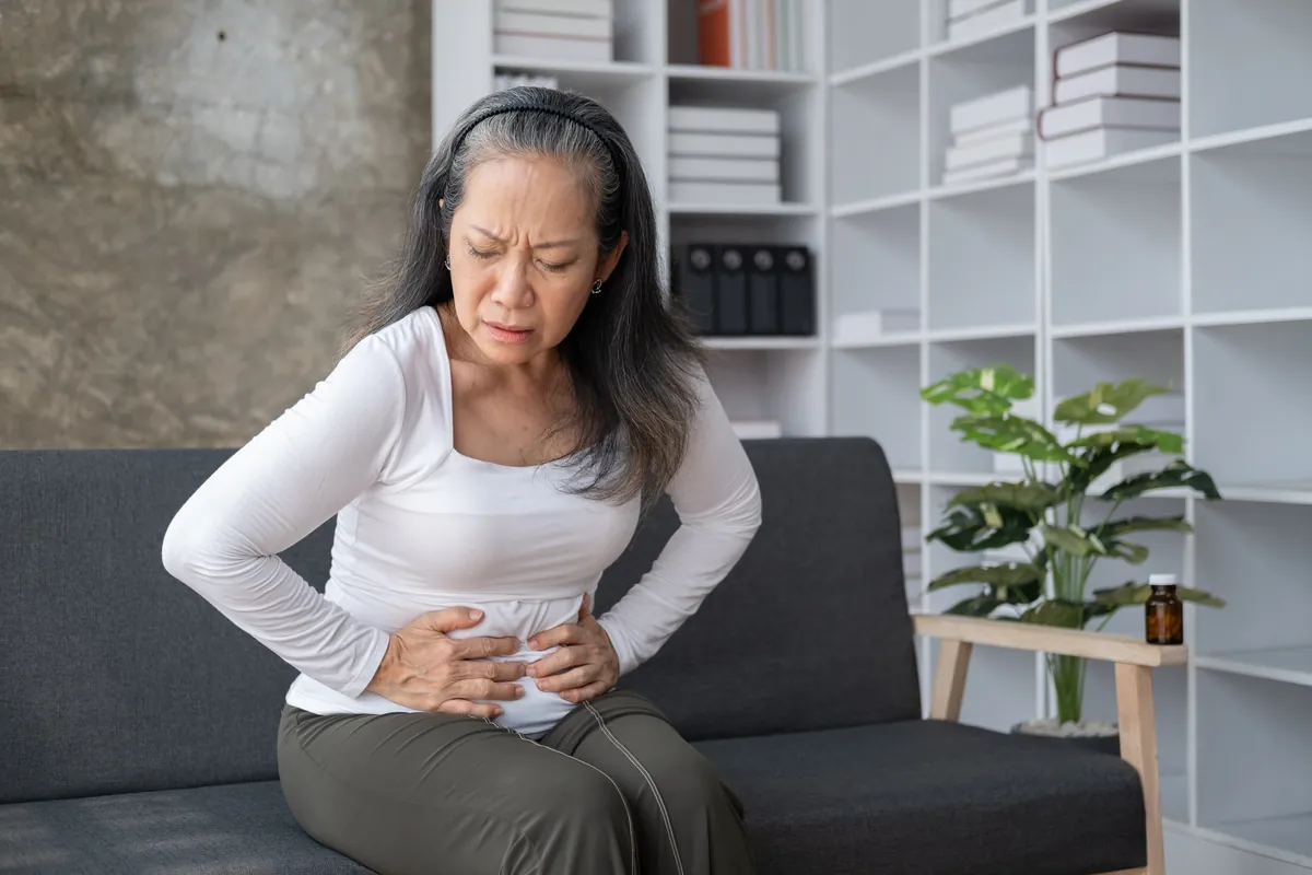 Woman sitting on a sofa holding her lower abdomen in pain